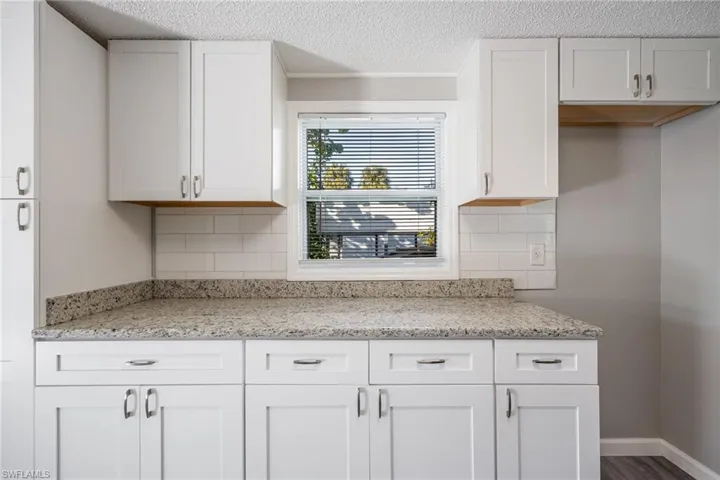 Kitchen featuring backsplash, a textured ceiling, light stone countertops, and white cabinets