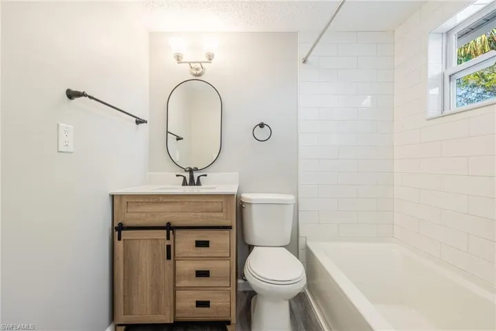 Full bathroom with tiled shower / bath combo, vanity, a textured ceiling, and toilet