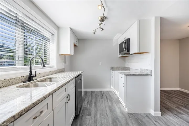 Kitchen with sink, white cabinetry, stainless steel appliances, wood-type flooring, and light stone countertops