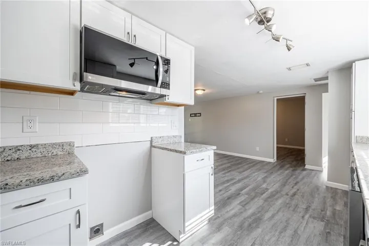 Kitchen featuring tasteful backsplash, light stone counters, white cabinets, and light wood-type flooring