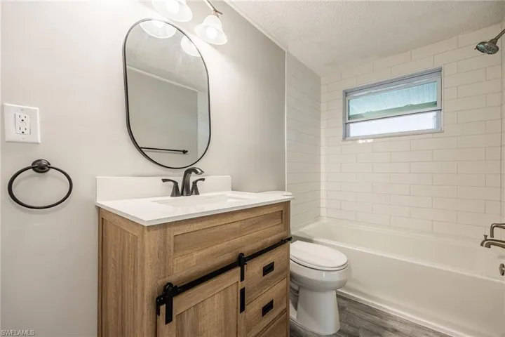 Full bathroom with vanity, wood-type flooring, a textured ceiling, toilet, and tiled shower / bath