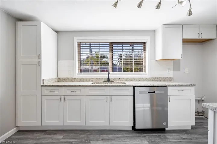 Kitchen with sink, backsplash, white cabinets, dark hardwood / wood-style flooring, and stainless steel dishwasher