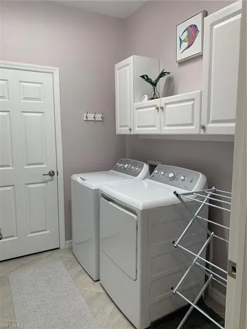 Laundry area with cabinets, separate washer and dryer, and light tile patterned flooring