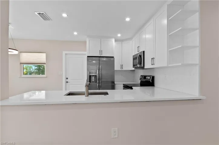 Kitchen with open shelves, light stone counters, stainless steel appliances, white cabinets, and a peninsula