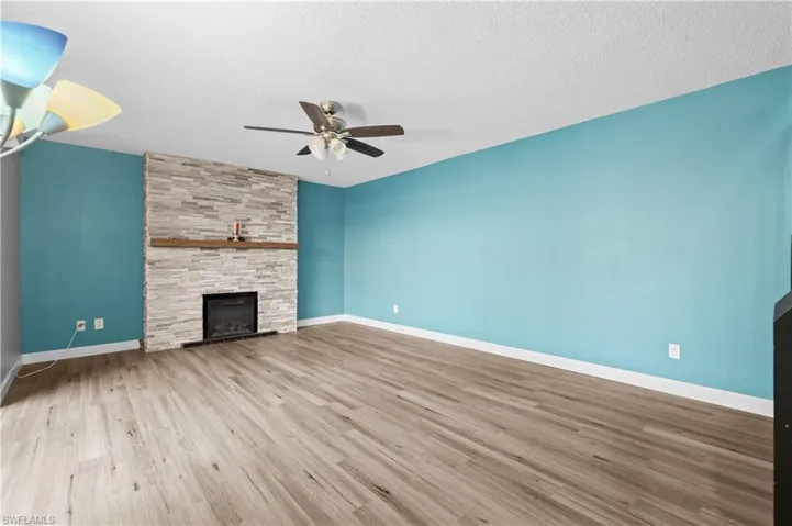 Unfurnished living room with wood finished floors, a fireplace, a textured ceiling, and a ceiling fan