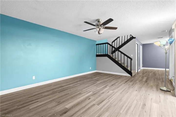 Unfurnished living room featuring a textured ceiling, stairway, light wood finished floors, and ceiling fan
