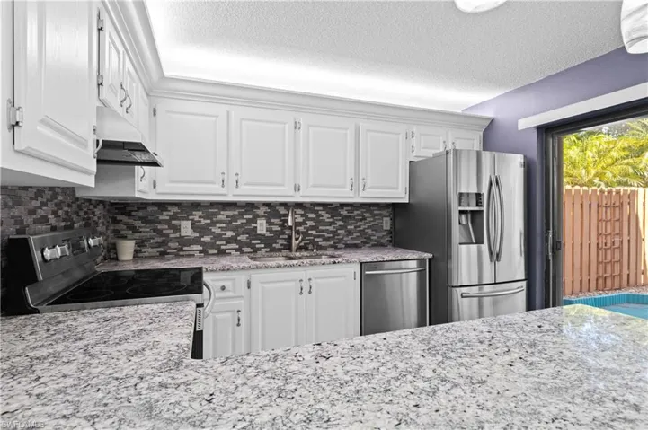 Kitchen featuring white cabinetry, stainless steel appliances, light stone countertops, a textured ceiling, and tasteful backsplash