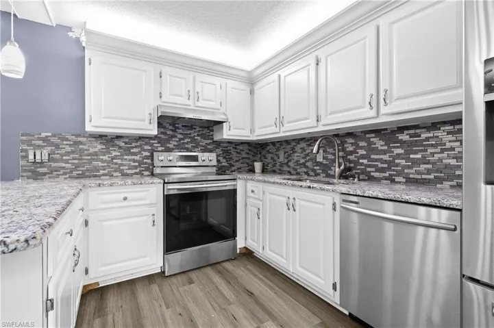 Kitchen with white cabinets, stainless steel appliances, a textured ceiling, and light stone countertops