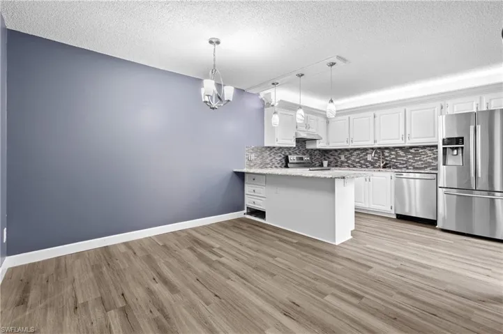 Kitchen with white cabinetry, stainless steel appliances, pendant lighting, a peninsula, and a textured ceiling