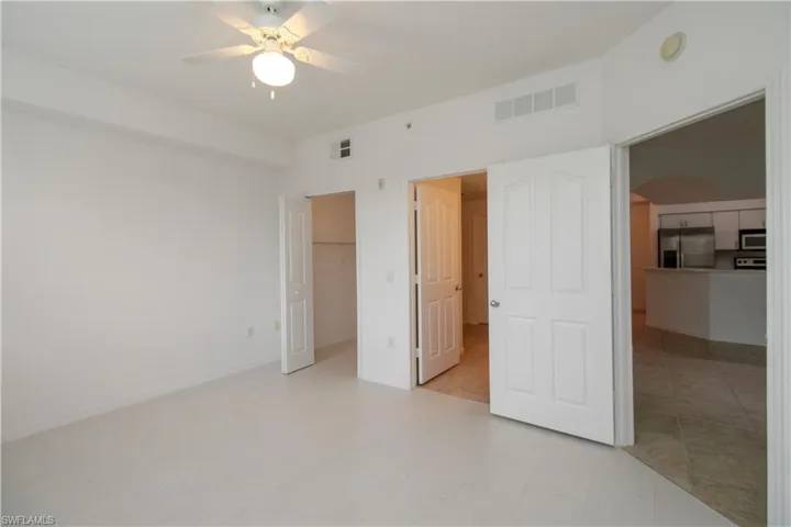 Unfurnished bedroom featuring stainless steel refrigerator with ice dispenser, a walk in closet, ceiling fan, light tile patterned floors, and a closet