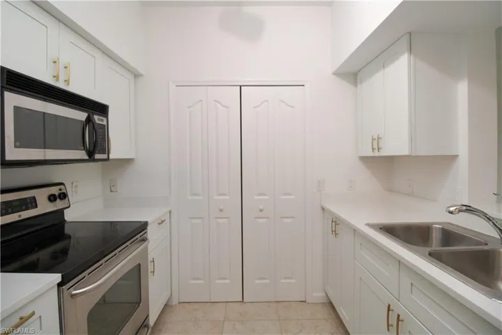 Kitchen with light tile patterned flooring, appliances with stainless steel finishes, white cabinetry, and sink