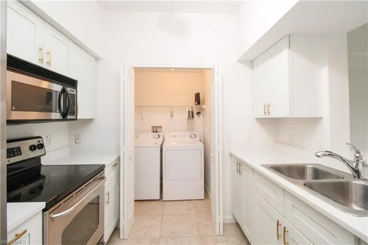 Kitchen with sink, light tile patterned flooring, washer and clothes dryer, white cabinets, and appliances with stainless steel finishes