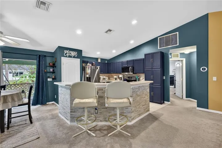 Kitchen featuring blue cabinets, light colored carpet, stainless steel appliances, light countertops, and a breakfast bar area
