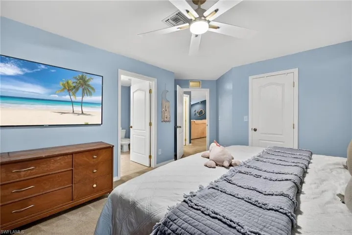 Bedroom with light colored carpet, a ceiling fan, ensuite bathroom, and a closet