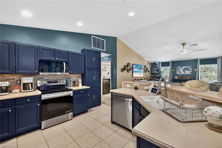 Kitchen featuring blue cabinetry, stainless steel appliances, light countertops, decorative backsplash, and vaulted ceiling