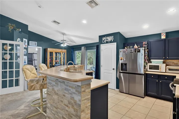 Kitchen with stainless steel refrigerator with ice dispenser, light countertops, a center island with sink, white microwave, and a kitchen breakfast bar