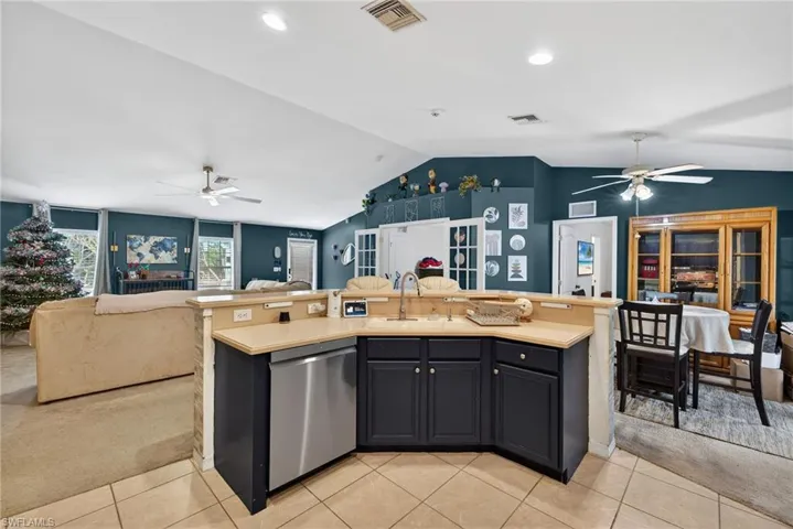 Kitchen featuring ceiling fan, open floor plan, a center island with sink, light carpet, and vaulted ceiling