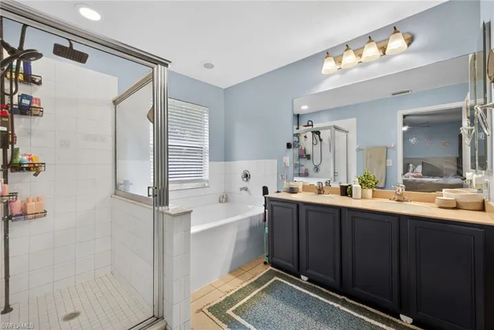 Bathroom featuring ensuite bathroom, double vanity, light tile patterned floors, a bath, and a stall shower