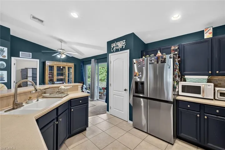 Kitchen featuring stainless steel fridge with ice dispenser, light countertops, white microwave, decorative backsplash, and lofted ceiling