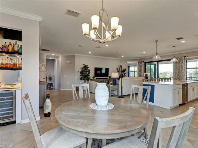 Open-concept living area with a central dining space, featuring a brushed nickel chandelier, crown molding, and tiled flooring