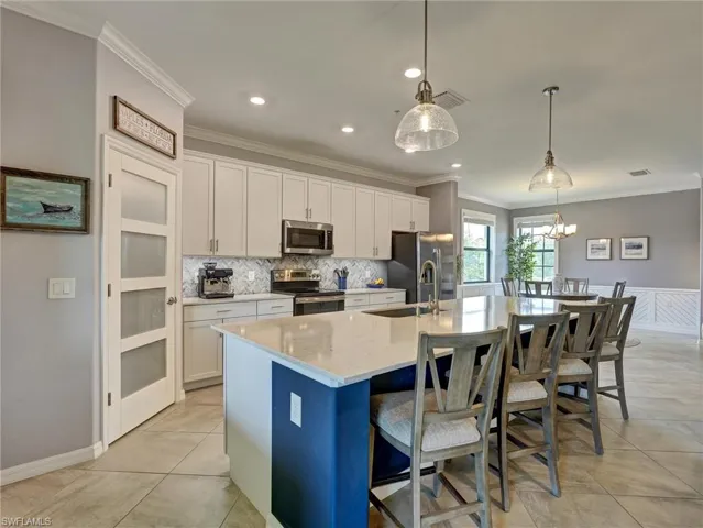 Gourmet kitchen featuring a large island with seating, stainless steel appliances, light cabinetry, a patterned backsplash, and tile flooring