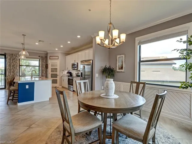 Open-concept living space with large format tile flooring, a kitchen island with seating, stainless steel appliances, white cabinetry, and a dining area featuring wainscoting and a decorative chandelier