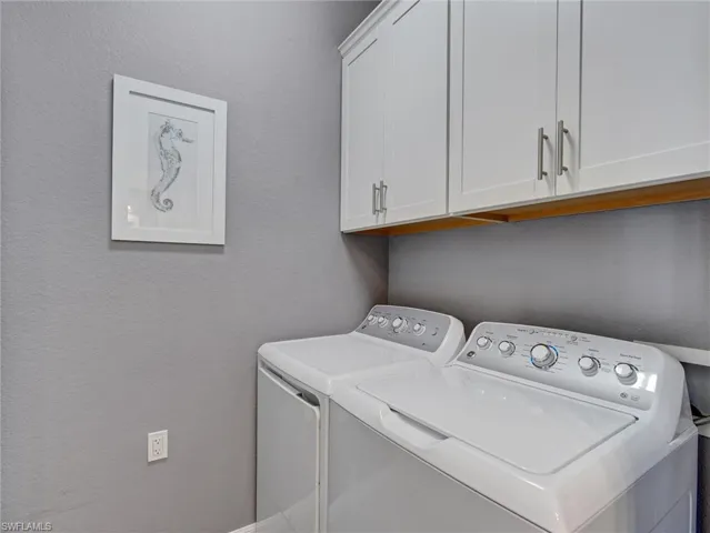 Dedicated laundry area featuring overhead white shaker cabinetry with brushed nickel hardware, a wood-finish shelf, and neutral wall paint