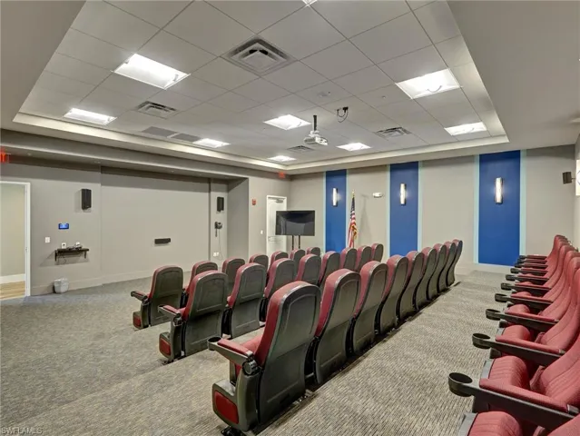Theater room featuring tiered seating, individual red upholstered chairs with cup holders, wall-mounted speakers, and a projector system