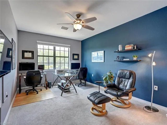 Carpeted room featuring a large window with grid panes, a ceiling fan with integrated lighting, and built-in wall shelving