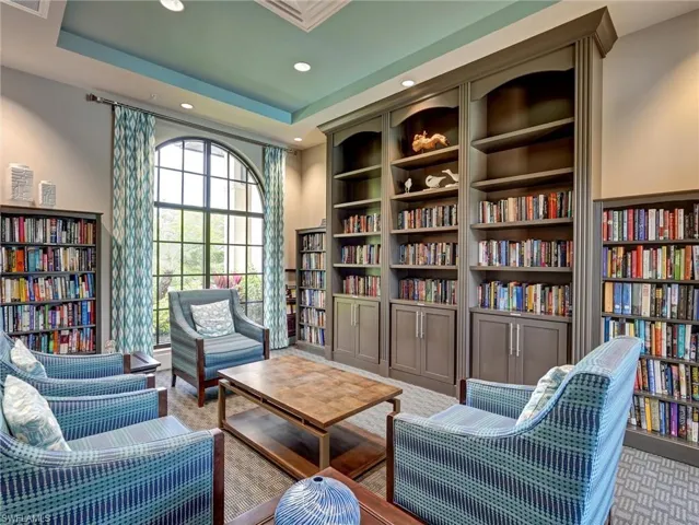 Spacious room featuring multiple built-in bookshelves, an arched window, patterned window treatments, and a recessed ceiling with accent lighting