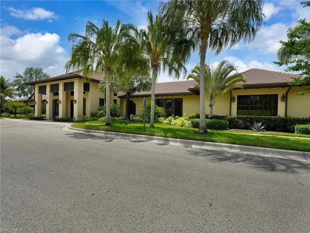 Exterior stucco residence featuring a tile roof, mature palm trees, manicured landscaping, decorative exterior lighting, and multi-pane windows