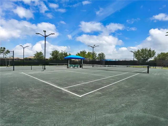Tennis court with multiple nets, integrated lighting fixtures, and a shaded seating area