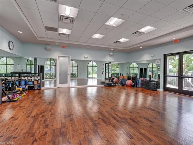 Spacious fitness studio featuring wood-finish flooring, full-wall mirrors, multiple arched windows, a drop ceiling with recessed lighting, and double glass-paneled exterior doors