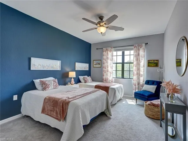 Spacious room featuring a large window with natural light, textured wall finishes, a ceiling fan with integrated lighting, and soft gray carpeting