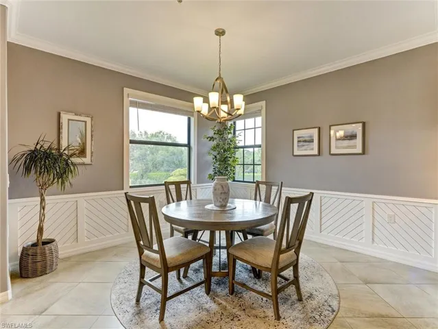 Dining area featuring a contemporary chandelier, two large windows, white wainscoting with diagonal accents, and neutral floor tiling