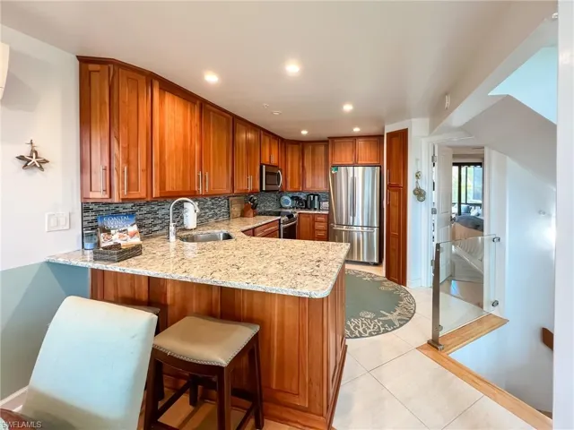 Kitchen with stainless steel appliances, kitchen peninsula, backsplash, sink, and light tile flooring
