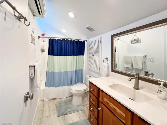 Full bathroom featuring shower / bath combo with shower curtain, a wall unit AC, vanity, and toilet