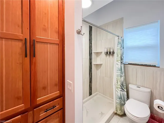Bathroom featuring tile flooring, a shower with shower curtain, toilet, and tile walls
