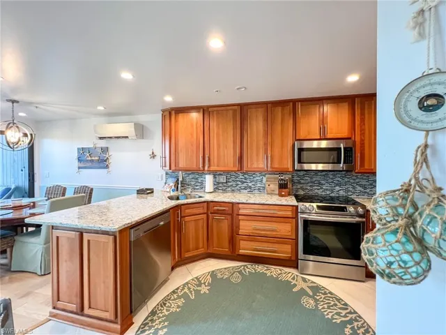 Kitchen with stainless steel appliances, kitchen peninsula, backsplash, sink, and light tile floors
