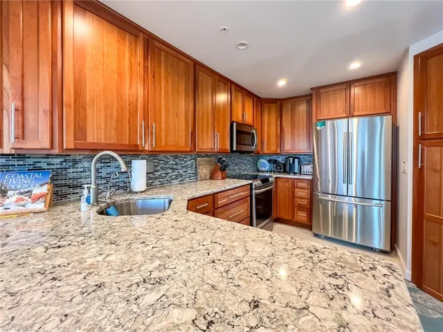 Kitchen featuring light stone counters, stainless steel appliances, backsplash, sink, and light tile floors
