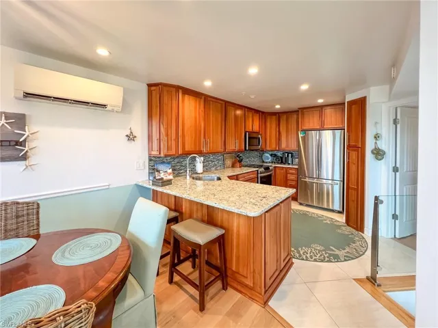 Kitchen featuring light stone countertops, appliances with stainless steel finishes, kitchen peninsula, backsplash, and sink