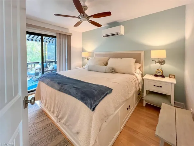 Bedroom featuring a wall mounted AC, ceiling fan, light wood-type flooring, and access to outside