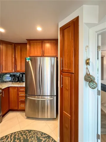 Kitchen featuring light stone countertops, backsplash, stainless steel fridge, and light tile floors