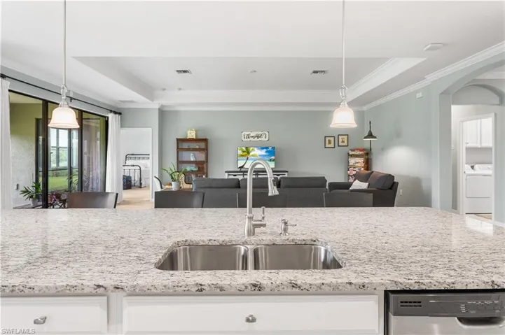 Kitchen featuring sink in island, dishwasher, a raised ceiling, and pendant lighting