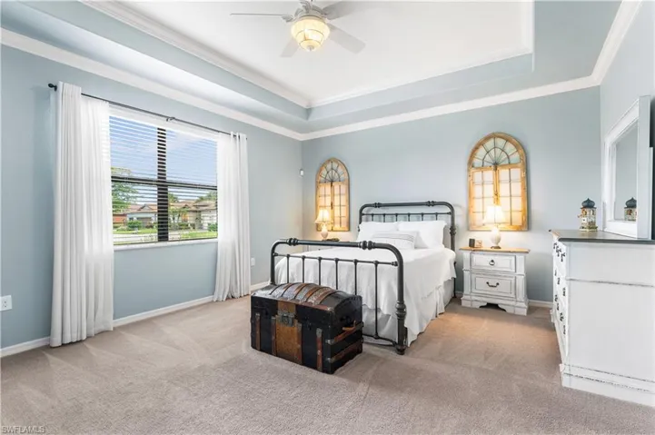 Bedroom featuring a raised ceiling, ceiling fan, light carpet, and ornamental molding