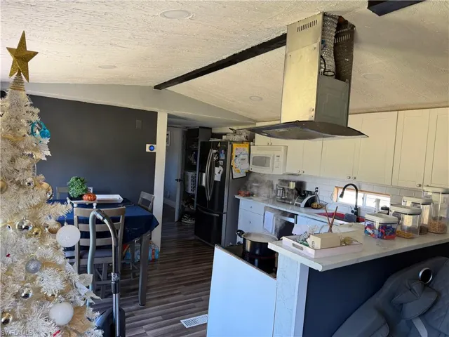 Kitchen with lofted ceiling, extractor fan, light countertops, white cabinetry, and stainless steel appliances