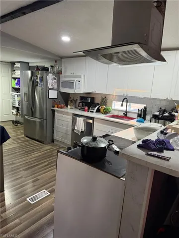 Kitchen featuring exhaust hood, white cabinetry, light countertops, appliances with stainless steel finishes, and dark wood-style flooring
