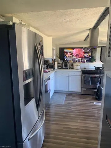 Kitchen with appliances with stainless steel finishes, white cabinetry, vaulted ceiling, light countertops, and dark wood-style flooring