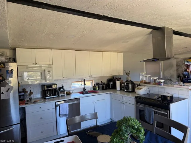 Kitchen featuring white cabinetry, appliances with stainless steel finishes, island exhaust hood, backsplash, and a peninsula