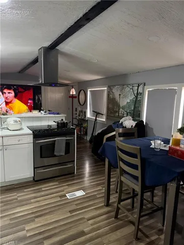 Kitchen with a textured ceiling, electric stove, white cabinets, light countertops, and ventilation hood
